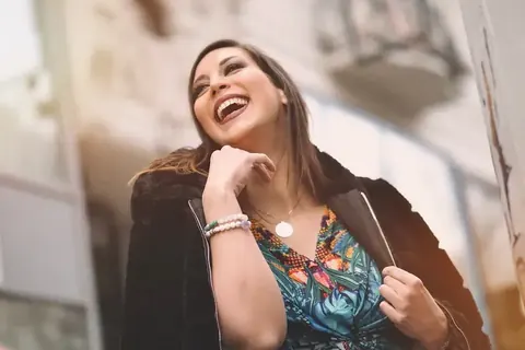 Ungezwungenes Personal-Branding-Porträt einer lachenden Frau in farbiger Kleidung und dunkler Jacke; der nach oben gerichtete Blick und der natürliche Ausdruck betonen…
