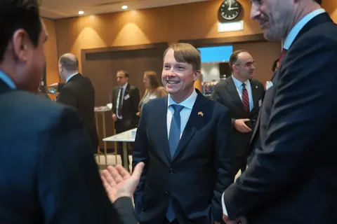 Ungezwungener Executive-Networking-Moment zwischen Anzugträgern bei einer internationalen Wirtschaftsveranstaltung; Blickkontakt und offene Gesten halten den…