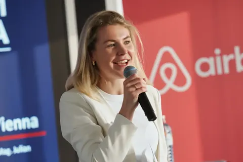 Rednerin mit Mikrofon neben Airbnb- und Vienna-Branding; expressive Präsentation und klare Bühnenfarben schaffen eine präzise redaktionelle Dokumentation des Vortrags.