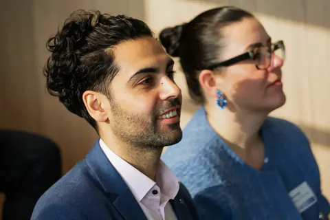Ungezwungene Publikumsreaktion bei einem professionellen Treffen mit zwei lächelnden, aufmerksam zuhörenden Gästen; das Bild dokumentiert Beteiligung, Atmosphäre und…
