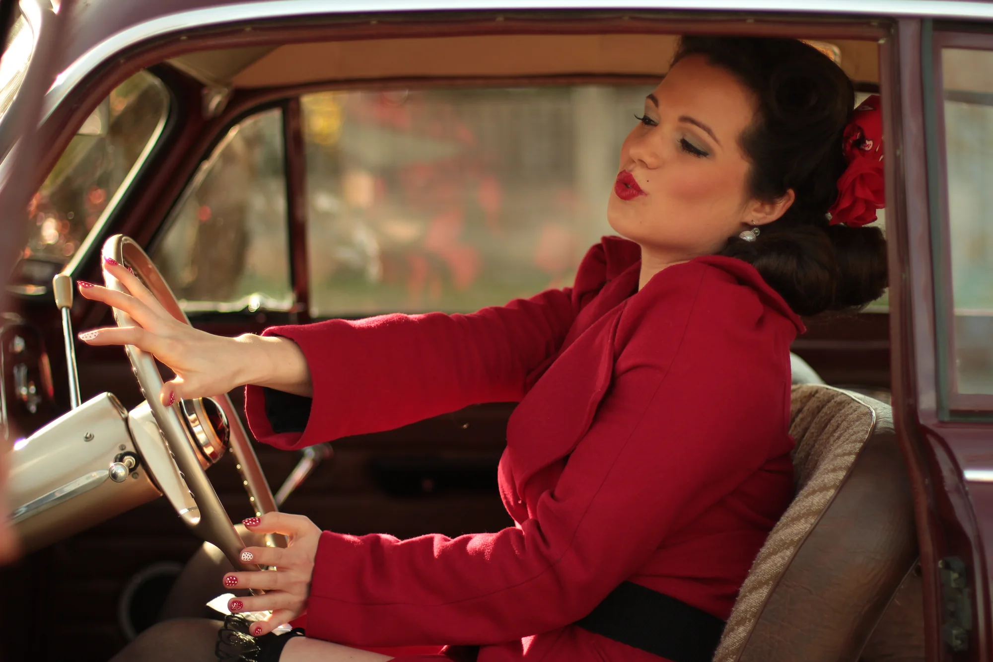 Frau in Rot am Steuer eines klassischen Automobils