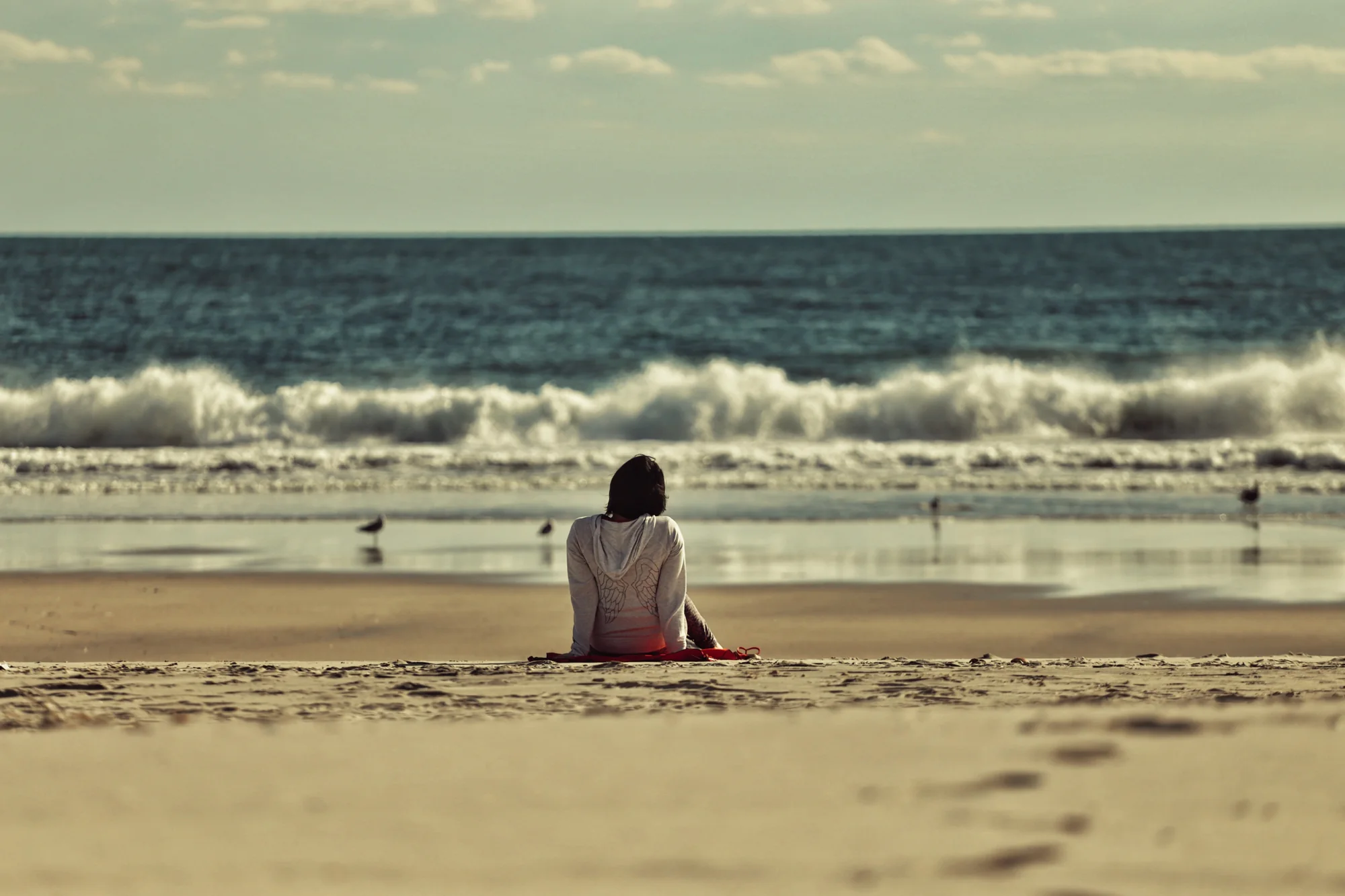 Einzelne sitzende Figur an einem weiten Strand mit Blick aufs Meer