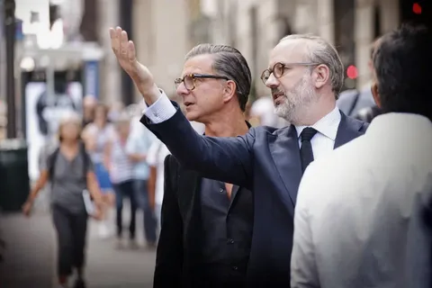 Ungezwungene Leadership-Aufnahme zweier Anzugträger im Gespräch auf einer Stadtstraße, wobei einer auf die Umgebung zeigt; das Bild verbindet Executive-Präsenz mit realem…