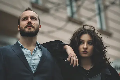 Umgebungs-Leadership-Porträt eines bärtigen Mannes im Anzug neben einer Frau mit dunklen Locken; tiefe urbane Perspektive deutet Partnerschaft, Ehrgeiz und gemeinsame…