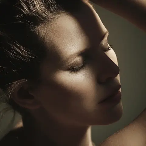Fine-Art-Profil einer Frau mit geschlossenen Augen in warmem gerichteten Licht; das skulptural modellierte Gesicht und der dunkle Hintergrund schaffen Stille, Intimität…